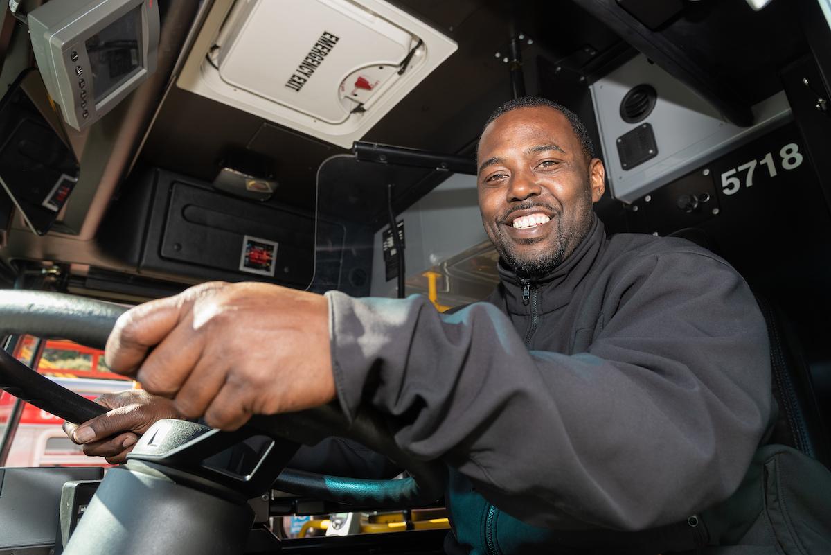 Muni operator smiling as they hold the steering wheel of a bus. Muni operator smiling as they hold the steering wheel of a bus.